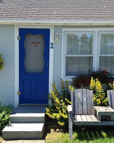 Blue-door guest cottage with Adirondack chairs and flower beds at one of Ohana's historic inns